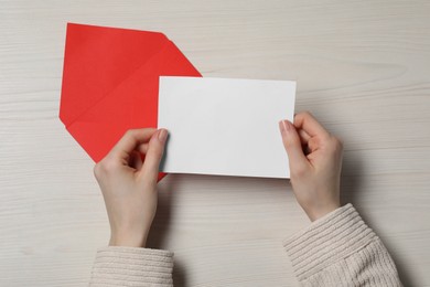 Woman with blank card at light wooden table, top view. Space for text