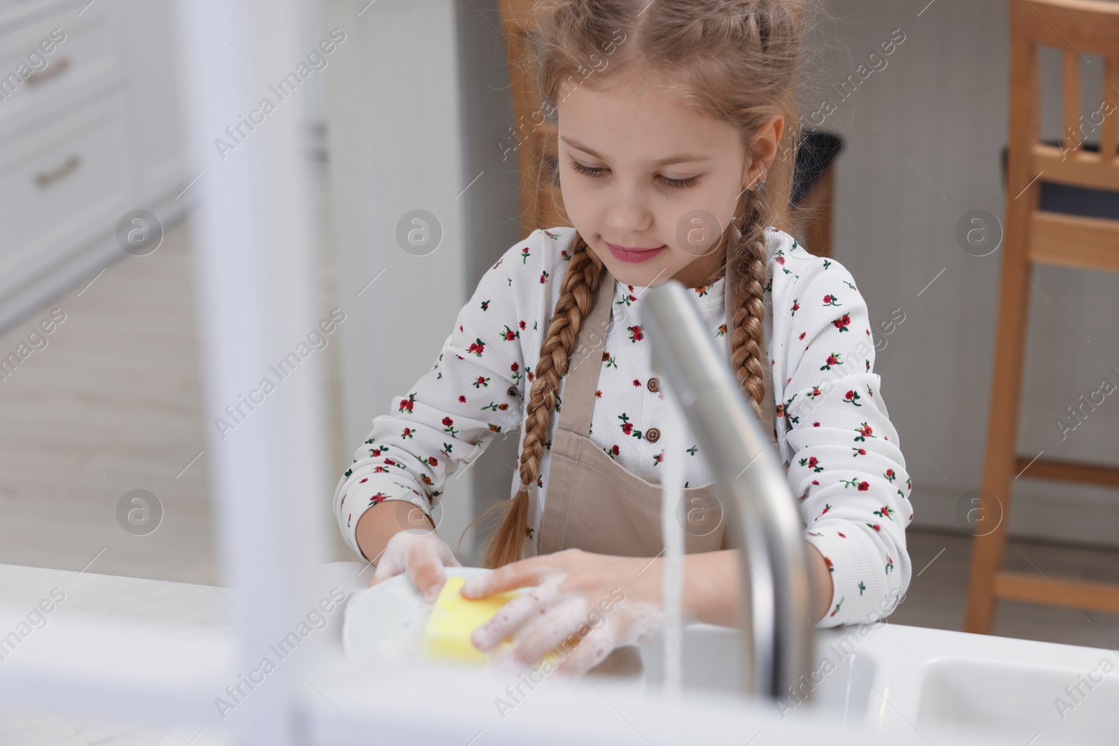 Photo of Little girl washing plate above sink in kitchen