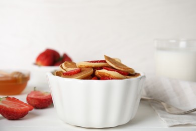 Photo of Delicious mini pancakes cereal with strawberries served on white wooden table