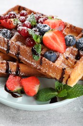 Photo of Delicious Belgian waffles with berries served on light grey table, closeup