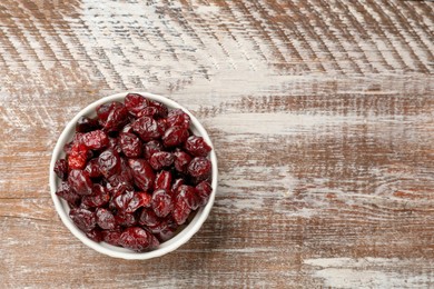 Tasty dried cranberries in bowl on rustic wooden table, top view. Space for text