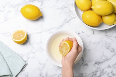 Photo of Woman squeezing lemon juice into bowl on table, top view