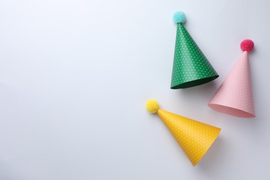Colorful party hats with pompoms on light background, top view. Space for text