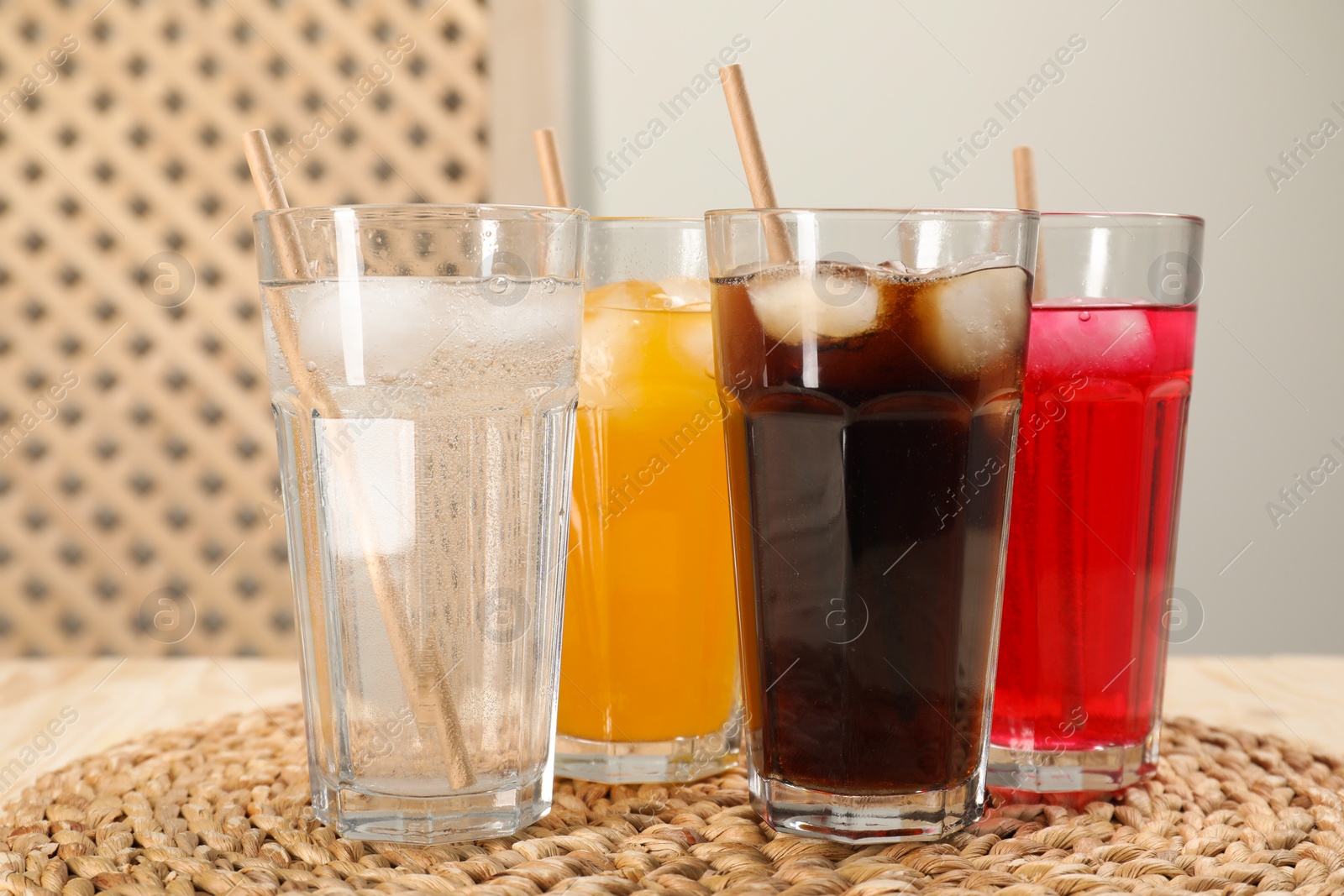 Photo of Glasses of different refreshing soda water with ice cubes and straws on wooden table