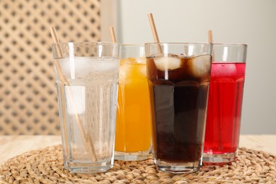 Photo of Glasses of different refreshing soda water with ice cubes and straws on wooden table