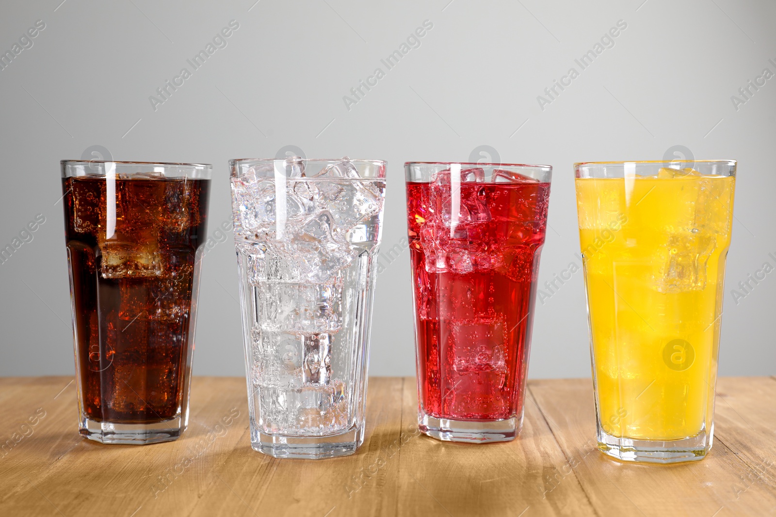 Photo of Glasses of different refreshing soda water with ice cubes on wooden table