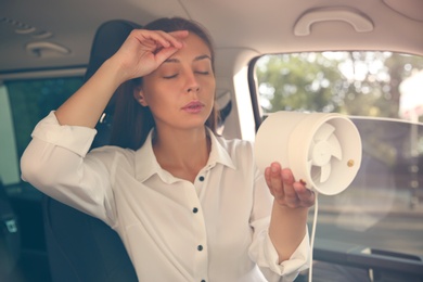 Photo of Young woman with portable fan suffering from heat in car on summer day