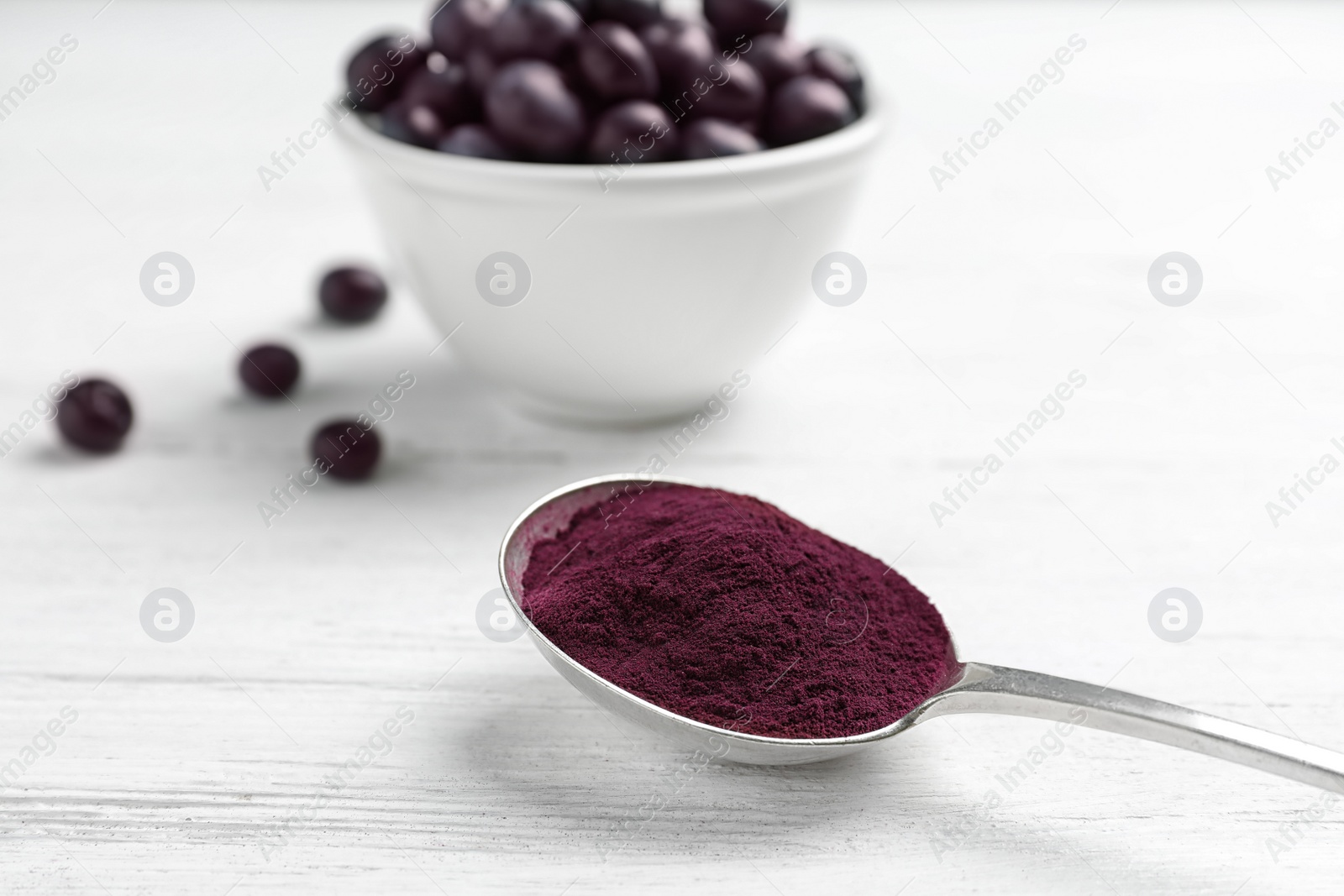 Photo of Spoon with acai powder and fresh berries on light wooden table