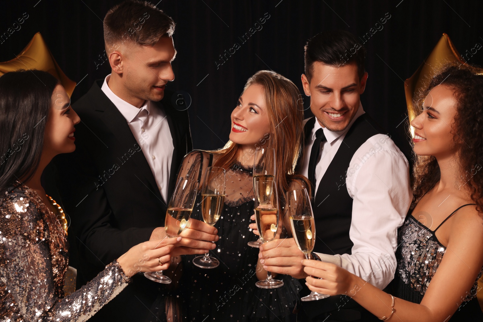 Photo of Happy friends with glasses of sparkling wine celebrating New Year on black background