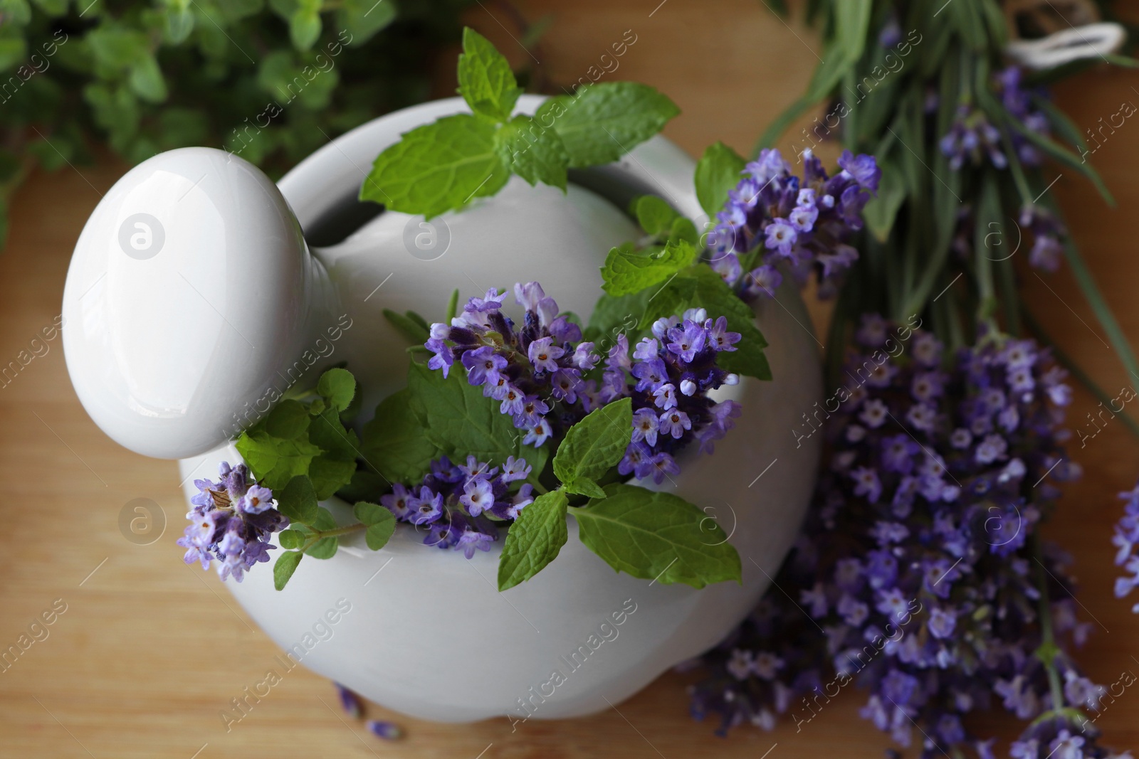 Photo of Mortar with fresh lavender flowers, mint and pestle on wooden table, closeup