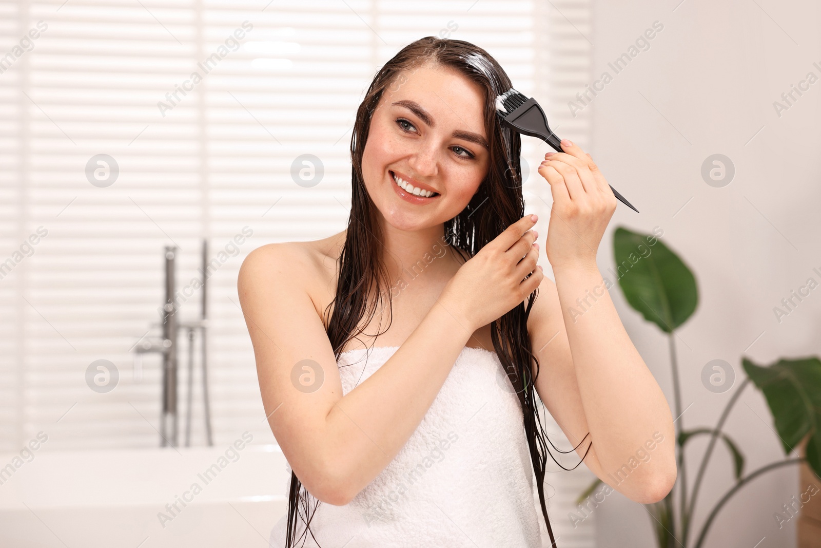 Photo of Young woman applying hair mask in bathroom