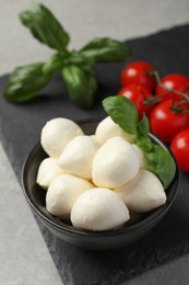 Photo of Delicious mozzarella balls, basil and tomatoes on light gray table, closeup