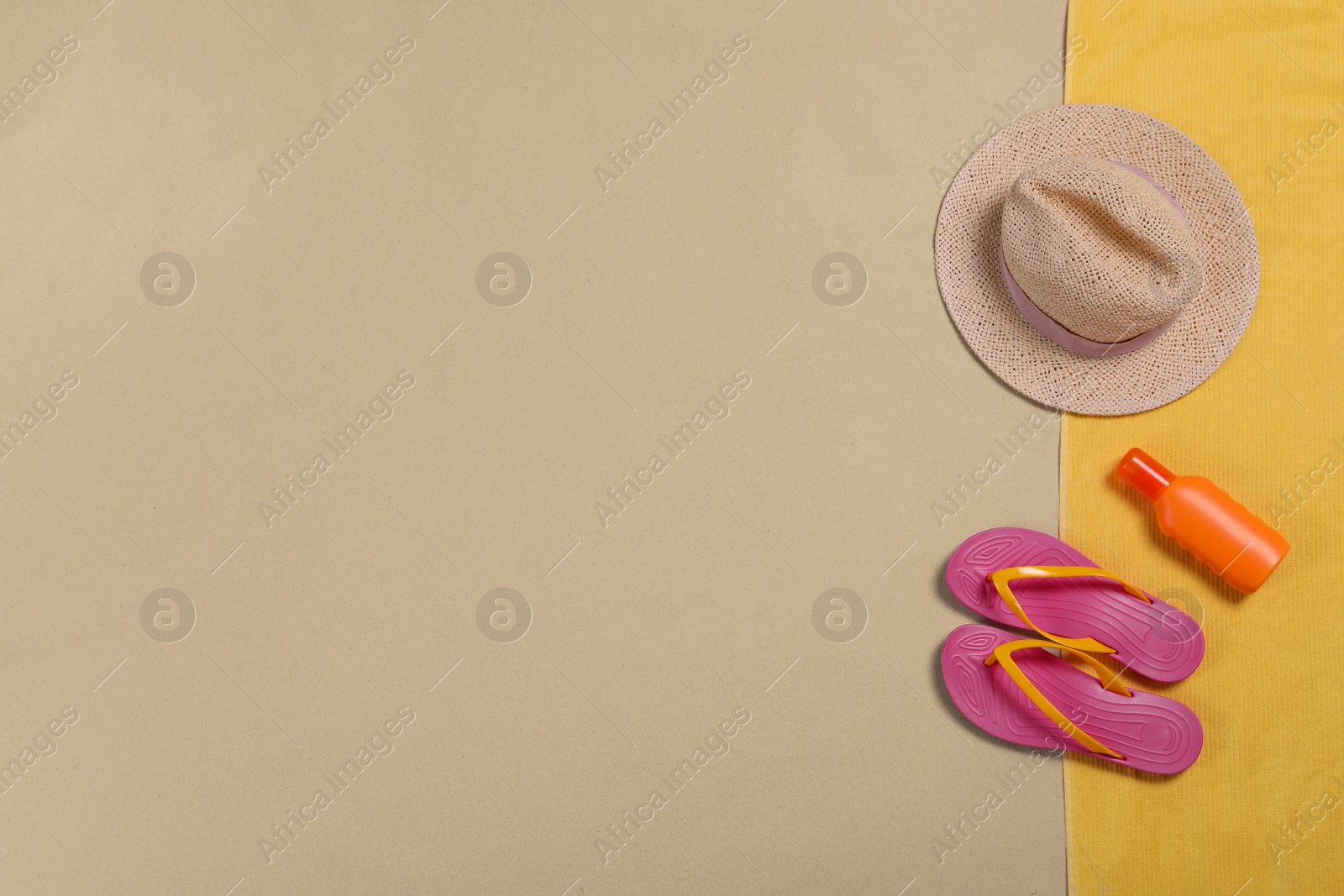 Photo of Beach towel, hat, sunscreen and flip flops on sand, flat lay. Space for text