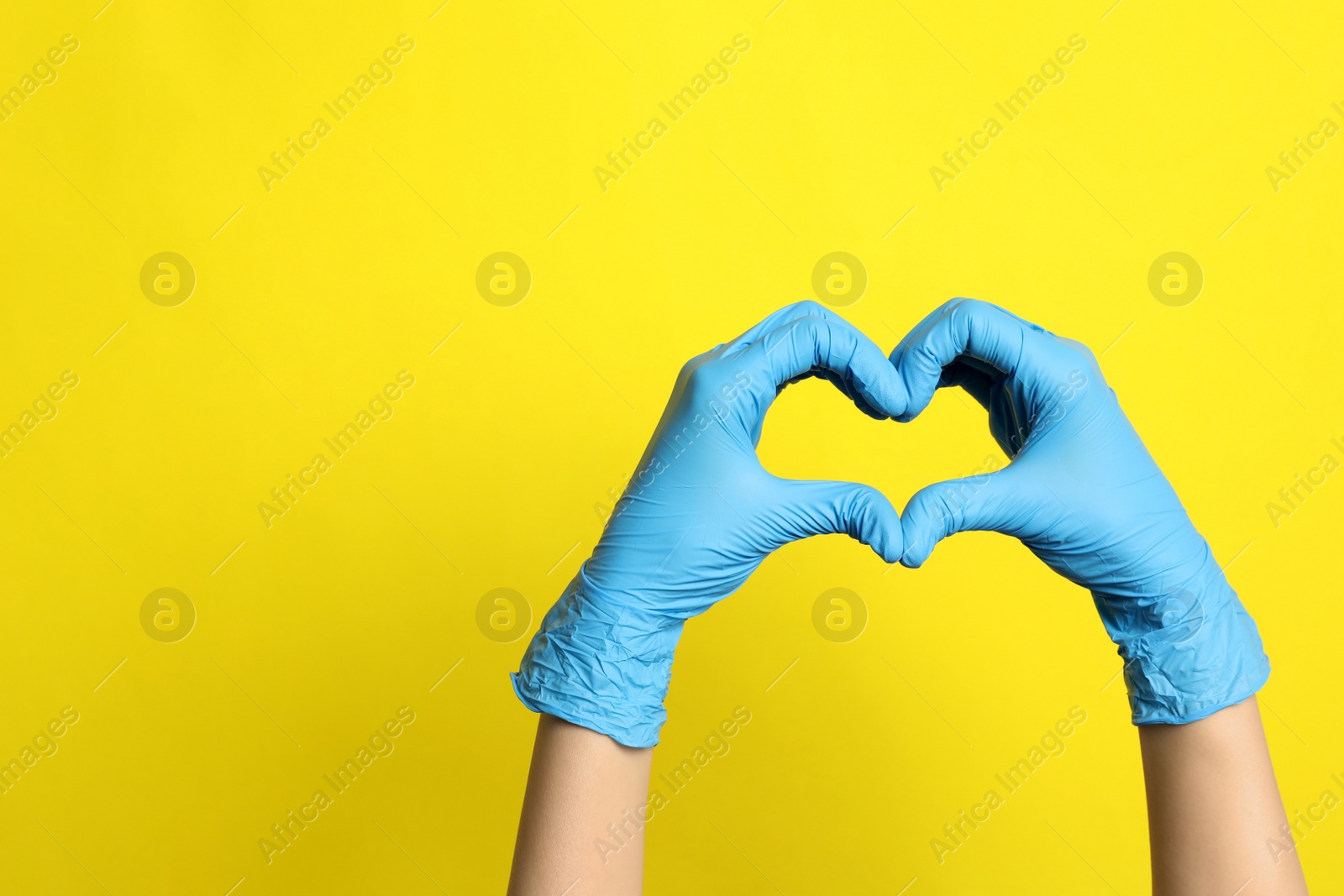 Photo of Doctor in medical gloves making heart with hands on yellow background, closeup. Space for text