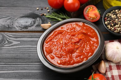 Photo of Homemade tomato sauce in bowl and fresh ingredients on black wooden table, space for text