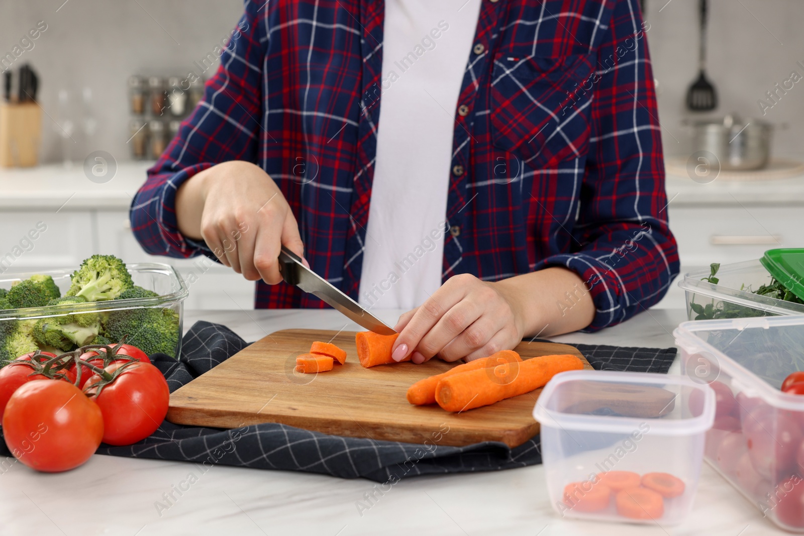 Photo of Woman cutting carrot near containers with fresh products on white marble table in kitchen, closeup. Food storage