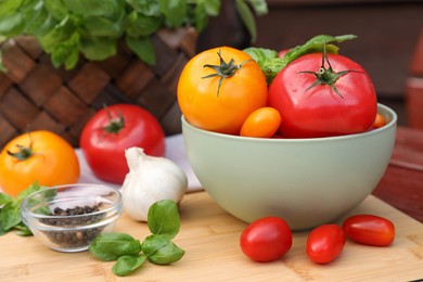 Different sorts of tomatoes with basil and peppercorns on wooden table