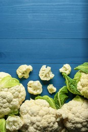 Photo of Fresh whole and cut cauliflowers on blue wooden table, top view. Space for text