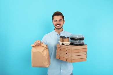 Young courier with different orders on color background. Food delivery service