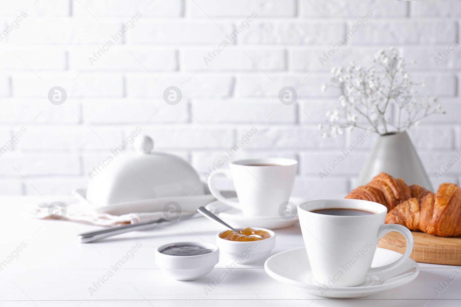 Photo of Cup of coffee, jam and croissants on white wooden table. Tasty breakfast