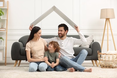 Photo of Housing concept. Happy husband holding plastic roof over his family while sitting on floor at home