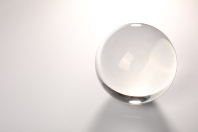 Photo of Transparent glass ball on light grey background. Space for text