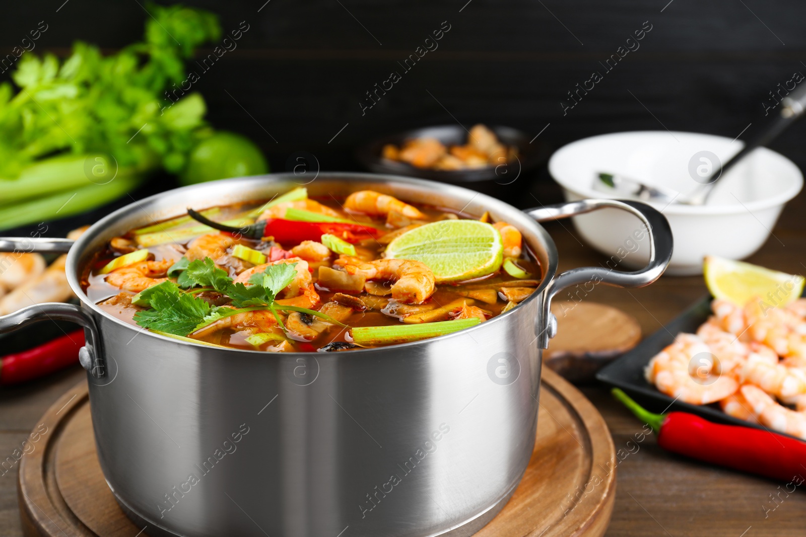 Photo of Saucepan with delicious Tom Yum soup and ingredients on wooden table