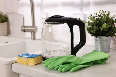 Photo of Cleaning electric kettle. Rubber gloves and sponge with foam on countertop in kitchen