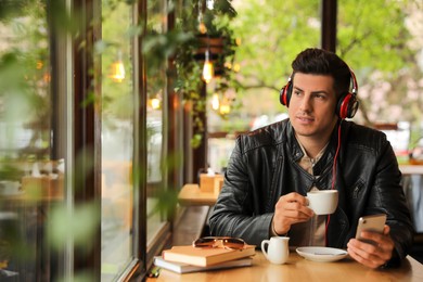 Man with smartphone listening to audiobook at table in cafe