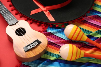 Photo of Mexican sombrero hat, maracas, guitar and colorful poncho on red background