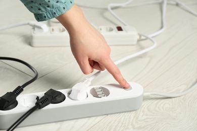 Photo of Woman pressing power button of extension cord on floor, closeup. Electrician's professional equipment