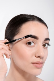 Beautiful woman with perfect eyebrows applying makeup on light background