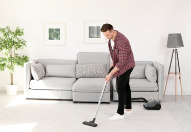 Photo of Young man removing dirt from carpet with vacuum cleaner at home