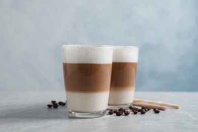 Glasses of delicious layered coffee, beans and straws on grey marble table against light background