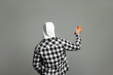 Photo of Man holding orange can of spray paint on grey background, back view