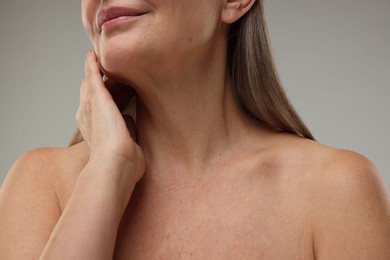 Photo of Mature woman touching her neck on grey background, closeup