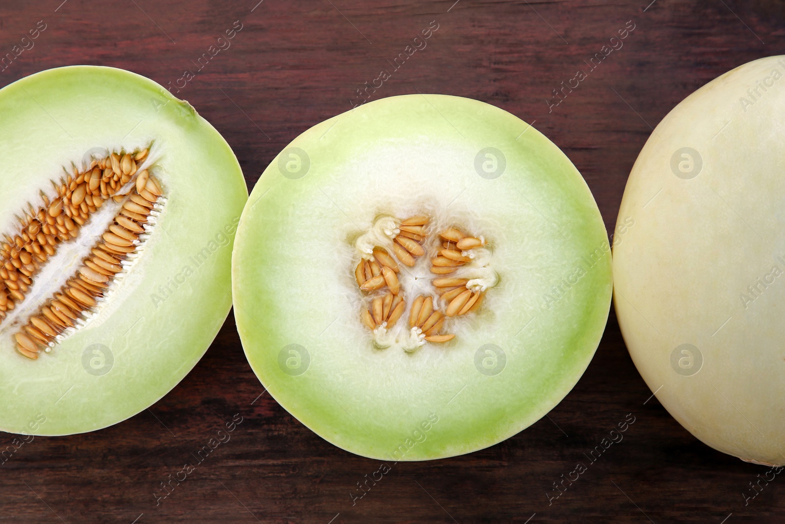 Photo of Cut and whole tasty ripe melons on wooden table, flat lay