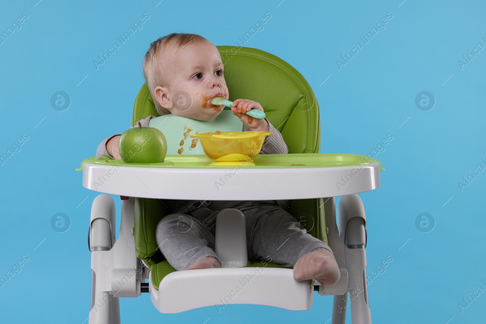 Photo of Cute little baby eating healthy food in high chair on light blue background