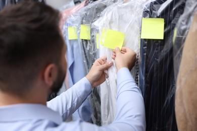 Photo of Dry-cleaning service. Worker sticking paper note onto clothes indoors, closeup