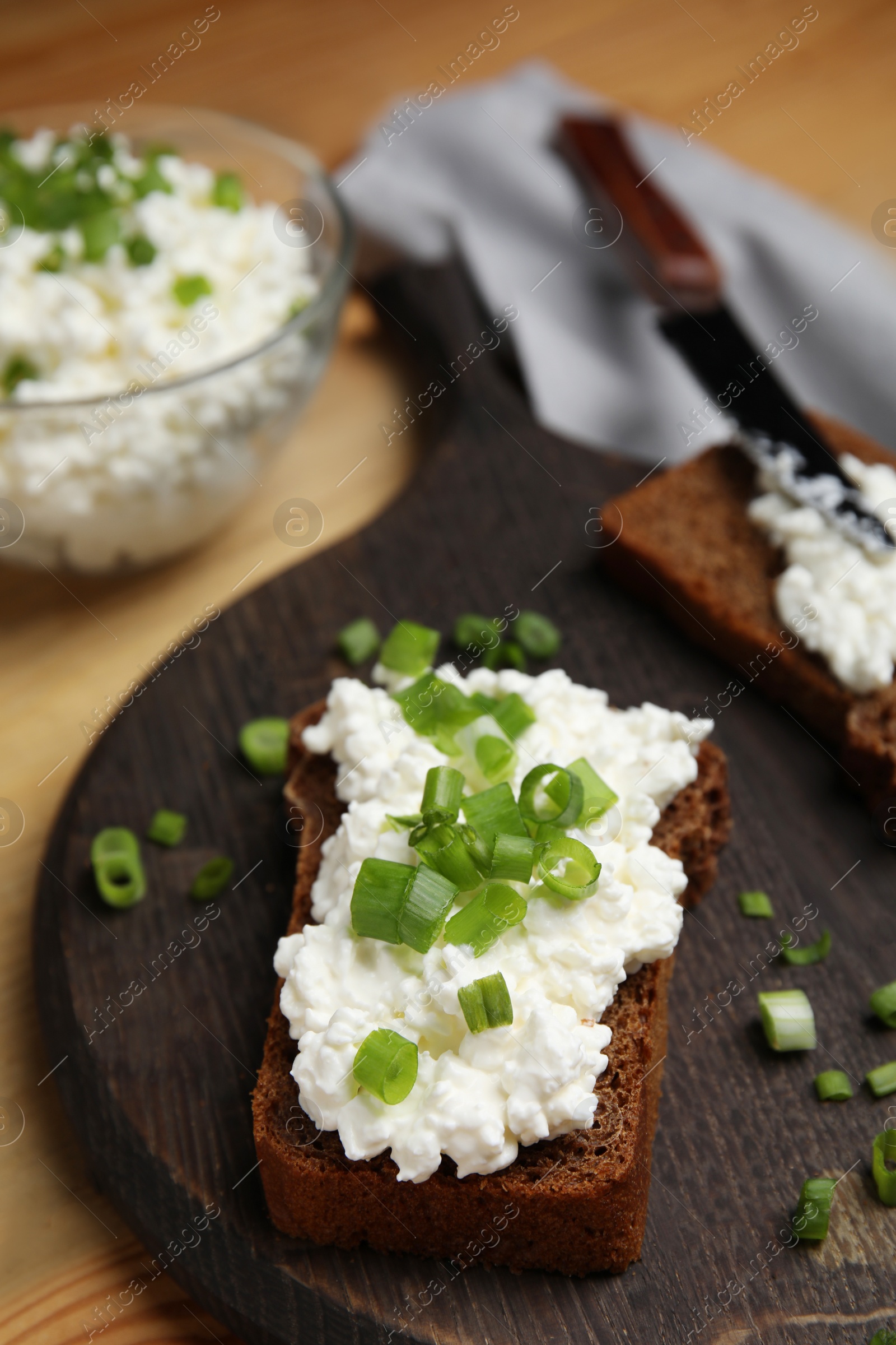 Photo of Bread with cottage cheese and green onion on wooden table, closeup