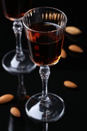 Photo of Liqueur glass with tasty amaretto and almonds on black table, closeup