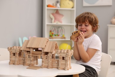 Photo of Little boy playing with wooden entry gate and car at white table in room. Child's toys
