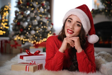 Beautiful woman wearing Santa hat with Christmas gifts on floor at home