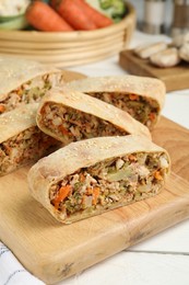 Photo of Cut tasty strudel with chicken and vegetables on white wooden table, closeup