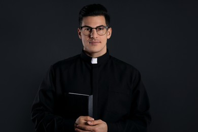 Priest in cassock with Bible on black background