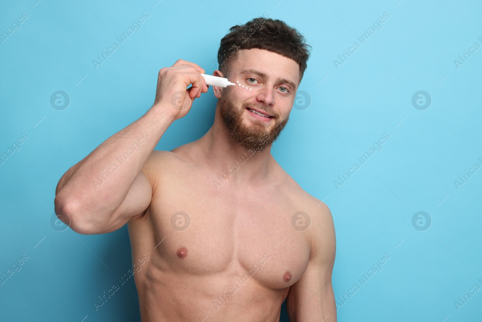 Photo of Handsome man applying moisturizing cream onto his face on light blue background