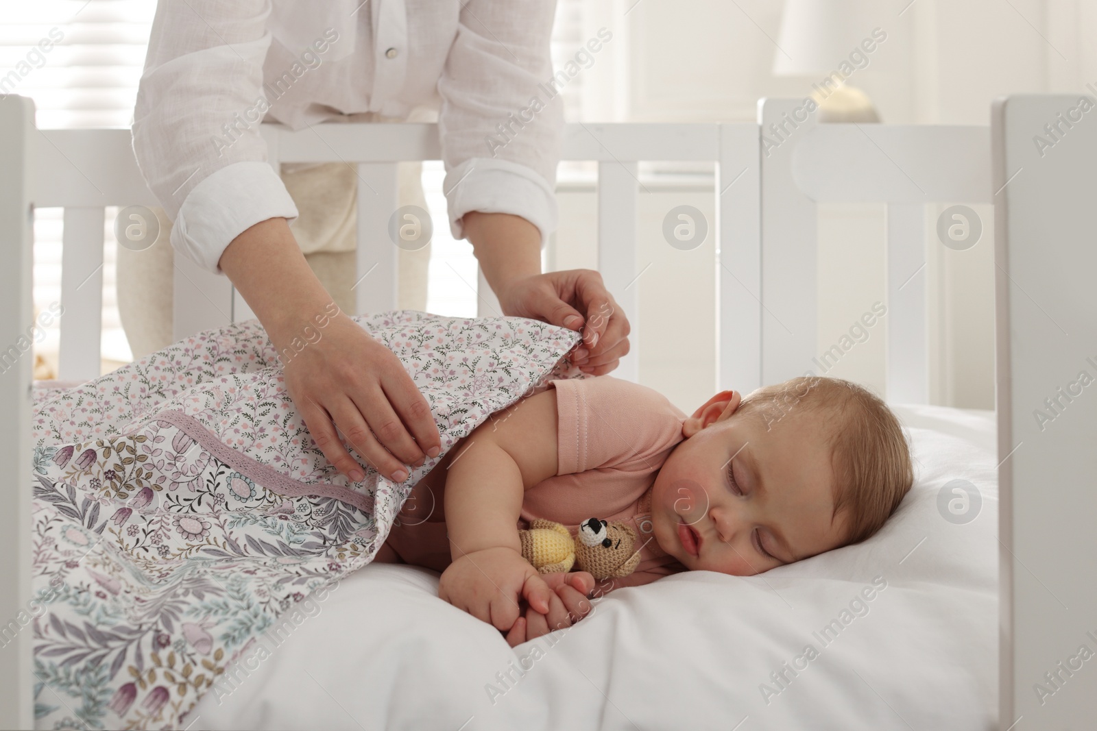 Photo of Mother covering her sleeping baby with blanket at home