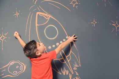 Photo of Cute little child playing with chalk rocket drawing on grey background