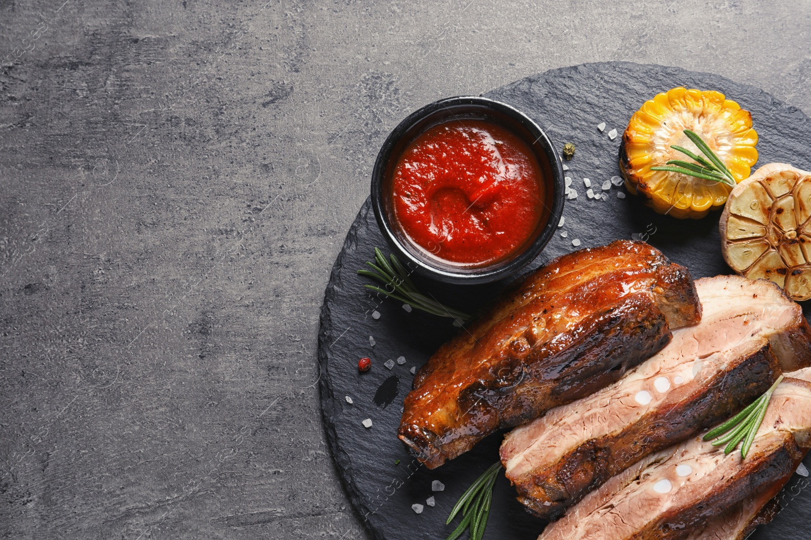 Photo of Slate plate with delicious barbecued meat on gray background. Space for text