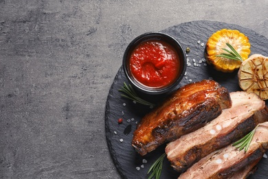Photo of Slate plate with delicious barbecued meat on gray background. Space for text